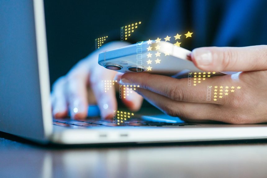 Person using a smartphone while typing on a laptop with digital feedback icons above