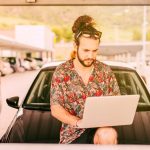 Hipster z laptopem siedzi na masce samochodu