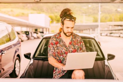 Hipster z laptopem siedzi na masce samochodu