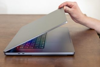 Ręka mężczyzny otwiera laptopa z wielokolorowym świecącym ekranem