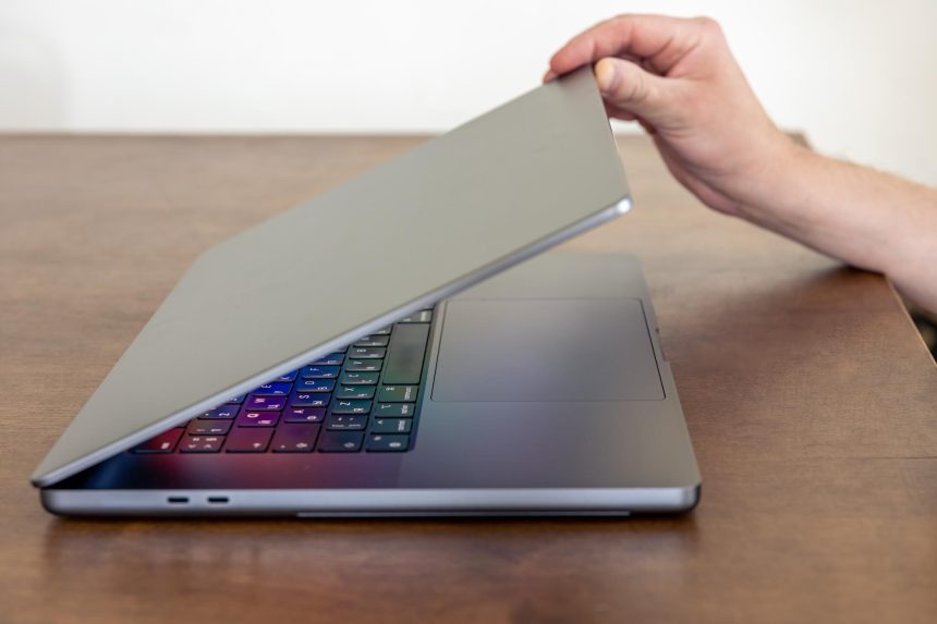 Ręka mężczyzny otwiera laptopa z wielokolorowym świecącym ekranem