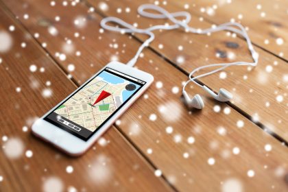 technologia, nawigacja, gadżet i koncepcja obiektu - zbliżenie białego smartfona i słuchawek na drewnianej powierzchni z mapą nawigatora GPS na ekranie