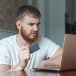 Nerwowy, smutny, zdezorientowany, młody człowiek, zestresowany, zaniepokojony, facet, który ma problemy z płaceniem za zakupy online.