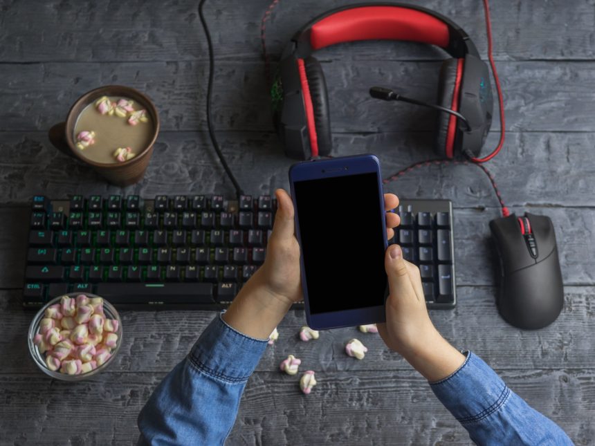 Dziewczyna trzyma telefon komórkowy na tle akcesoriów komputerowych, kawy i pianki