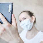 Dziewczyna w masce medycznej zostaje poddana kwarantannie w domu i bierze selfie na smartfonie.