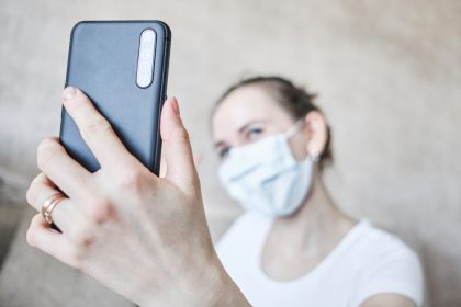 Dziewczyna w masce medycznej zostaje poddana kwarantannie w domu i bierze selfie na smartfonie.