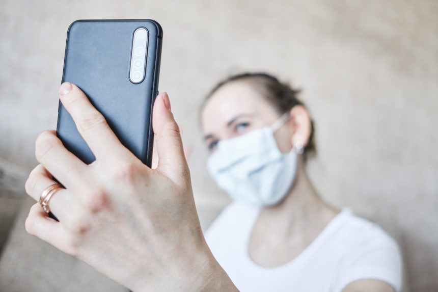 Dziewczyna w masce medycznej zostaje poddana kwarantannie w domu i bierze selfie na smartfonie.