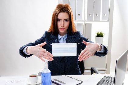 kobieta biznesu przy biurku z komputerem trzyma w dłoniach medyczną maskę