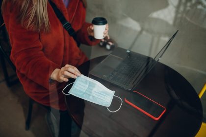 Maska medyczna, dłonie, stół, laptop i telefon komórkowy
