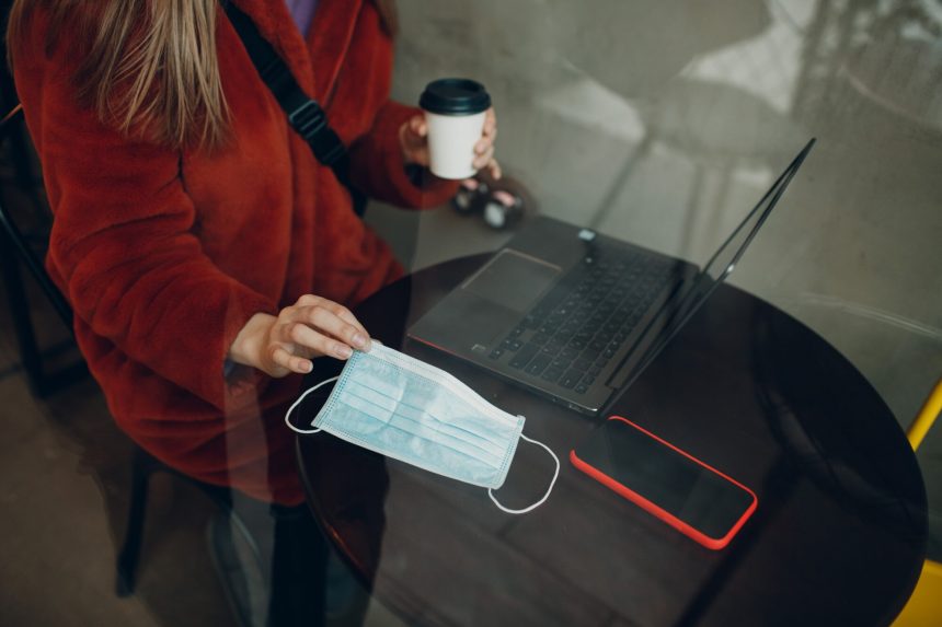 Maska medyczna, dłonie, stół, laptop i telefon komórkowy