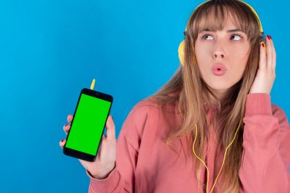 Piękna młoda kobieta słucha muzyki przez słuchawki i okulary przeciwsłoneczne, chromowany ekran telefonu komórkowego