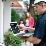 Wykwalifikowany technik pracujący przy instalacji domowej stacji ładowania pojazdów elektrycznych, rozwiązujący problemy i konfigurujący system ładowania za pomocą laptopa do pojazdów elektrycznych w domu z obecnymi w rodzinie urządzeniami Synchronos