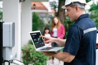 Wykwalifikowany technik pracujący przy instalacji domowej stacji ładowania pojazdów elektrycznych, rozwiązujący problemy i konfigurujący system ładowania za pomocą laptopa do pojazdów elektrycznych w domu z obecnymi w rodzinie urządzeniami Synchronos