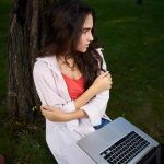 Młoda kobieta używająca laptopa siedząc na boisku