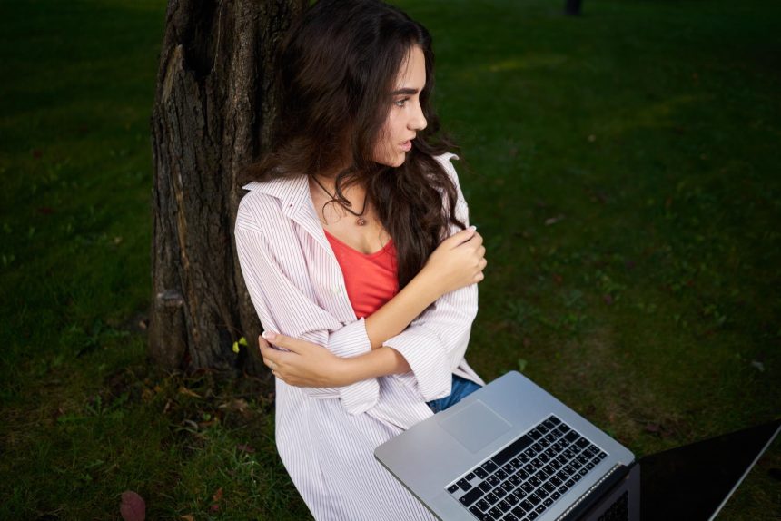 Młoda kobieta używająca laptopa siedząc na boisku