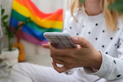Młoda milenijna hippie siedząca na balkonie z telefonem komórkowym lgbtq tęcza flaga