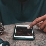 Środkowa część człowieka używającego telefonu komórkowego przez stożek sosny na stole