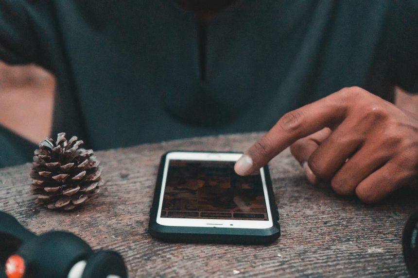 Środkowa część człowieka używającego telefonu komórkowego przez stożek sosny na stole